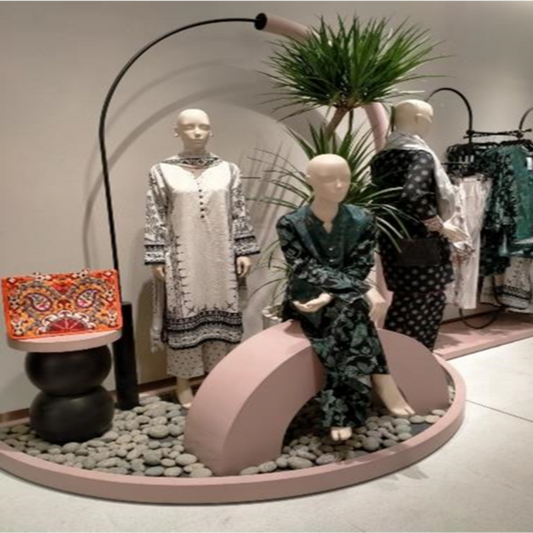 Mannequins dressed in patterned outfits with a decorative plant and colorful bag in a store setting.