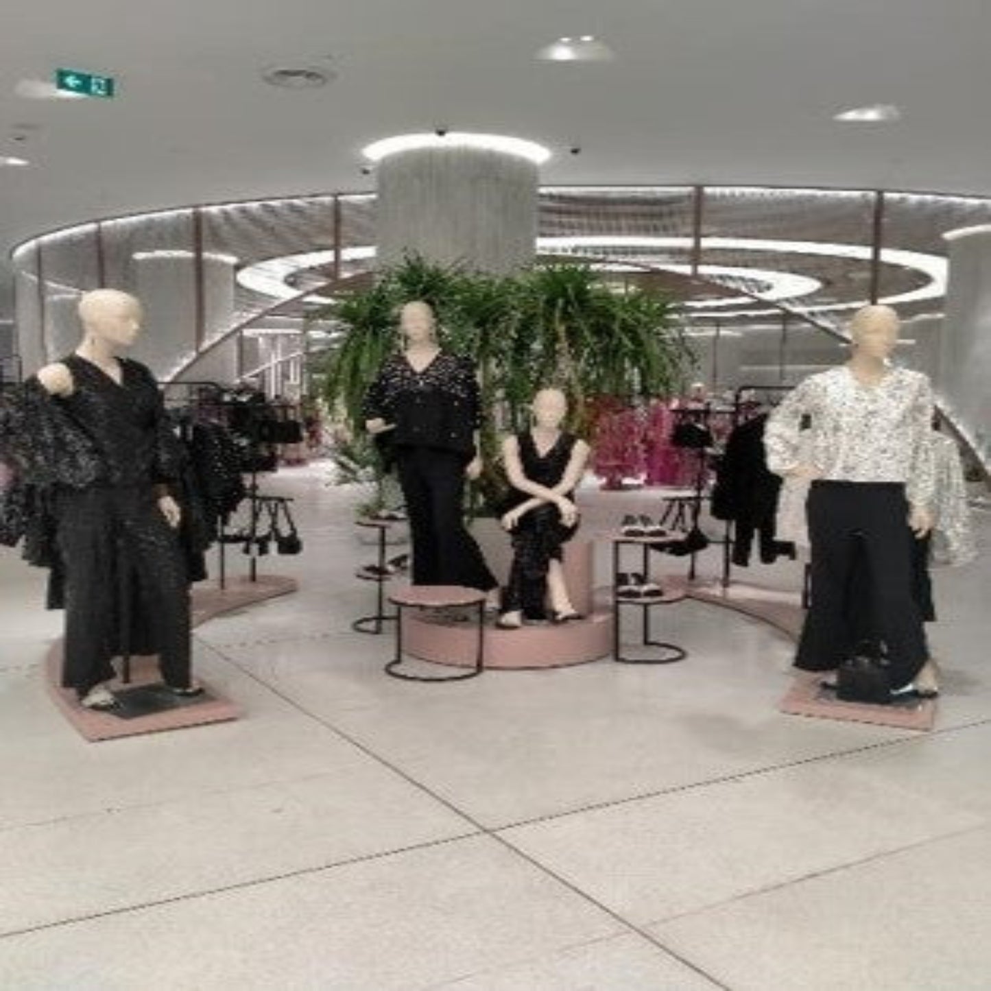 Mannequins dressed in black and white outfits in a store setting with plants and mirrors.