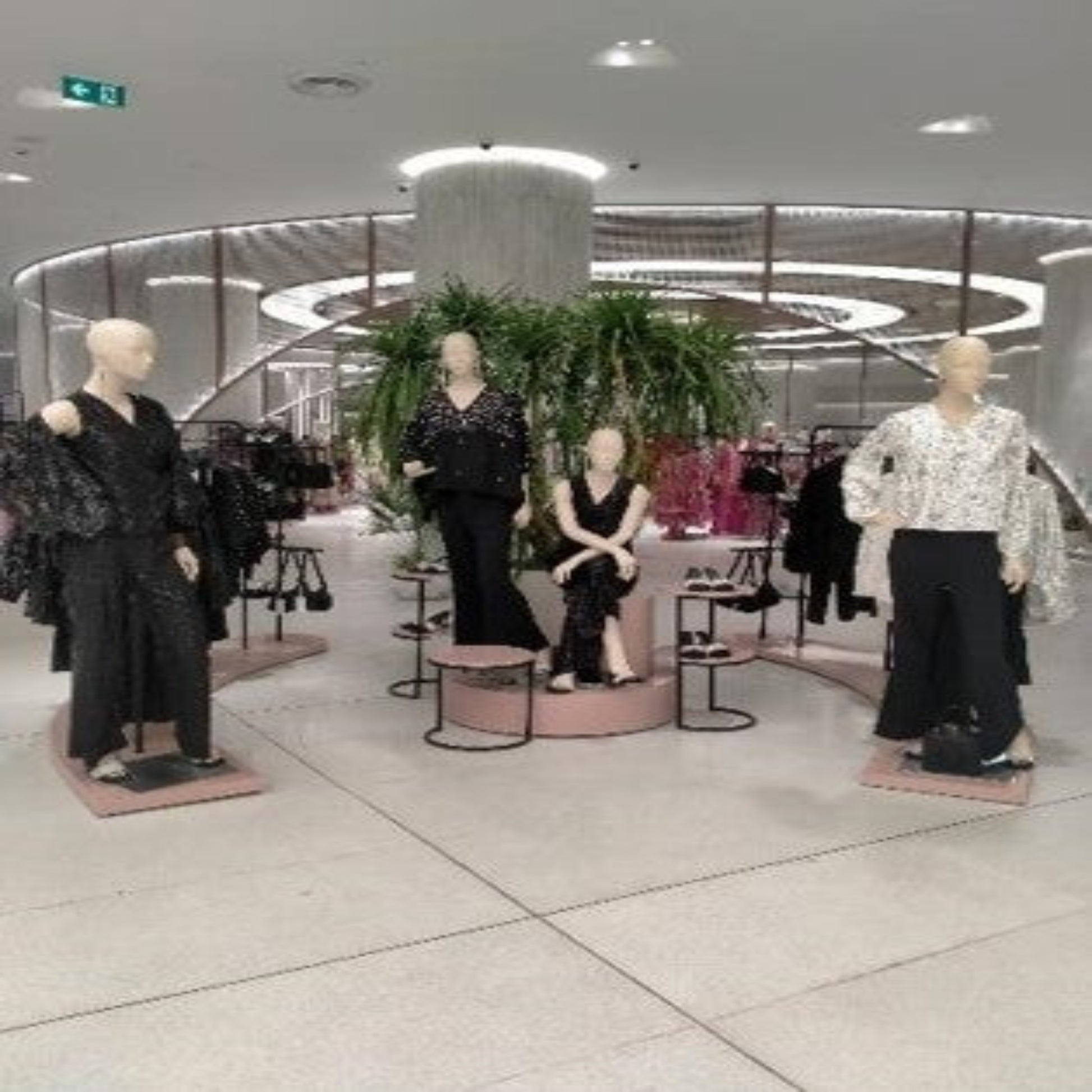 Mannequins dressed in black and white outfits in a store setting with plants and mirrors.