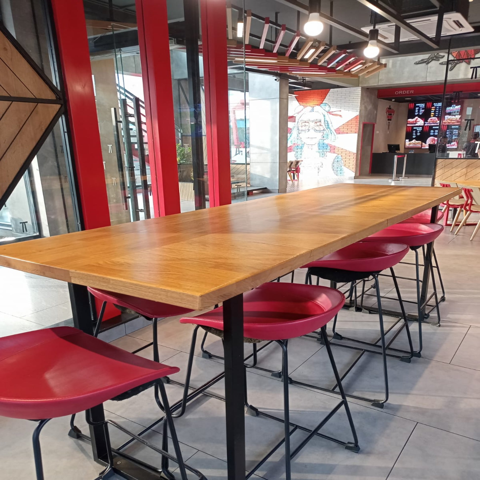 Kfc Pakistan, wooden dining table with red chairs in a modern indoor setting.