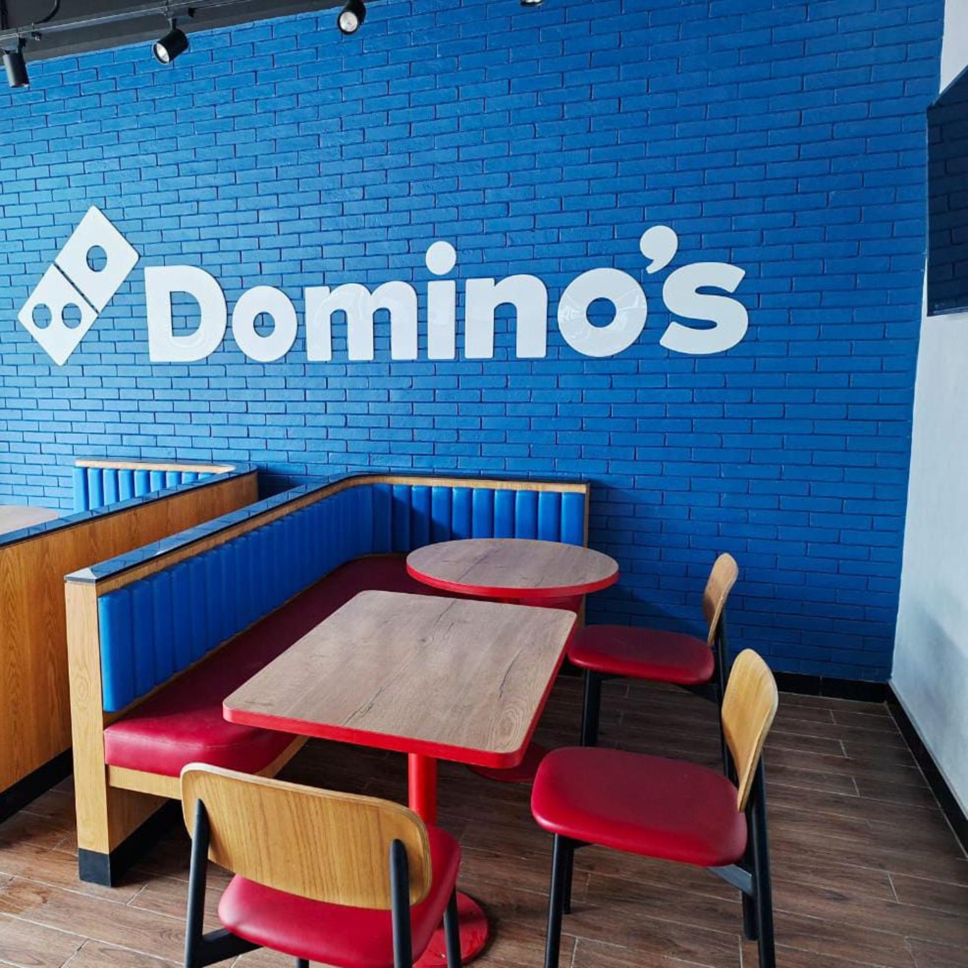 Domino's restaurant interior with blue brick wall and wooden tables.