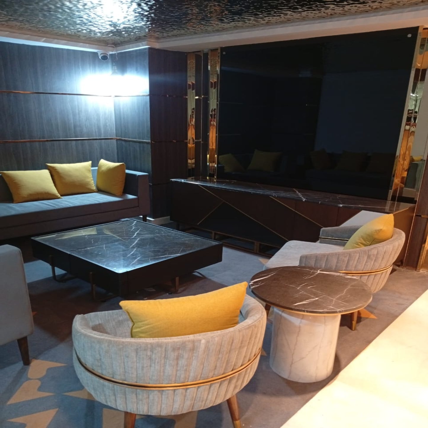 Modern living room with a large TV, couch, and chairs with yellow cushions.