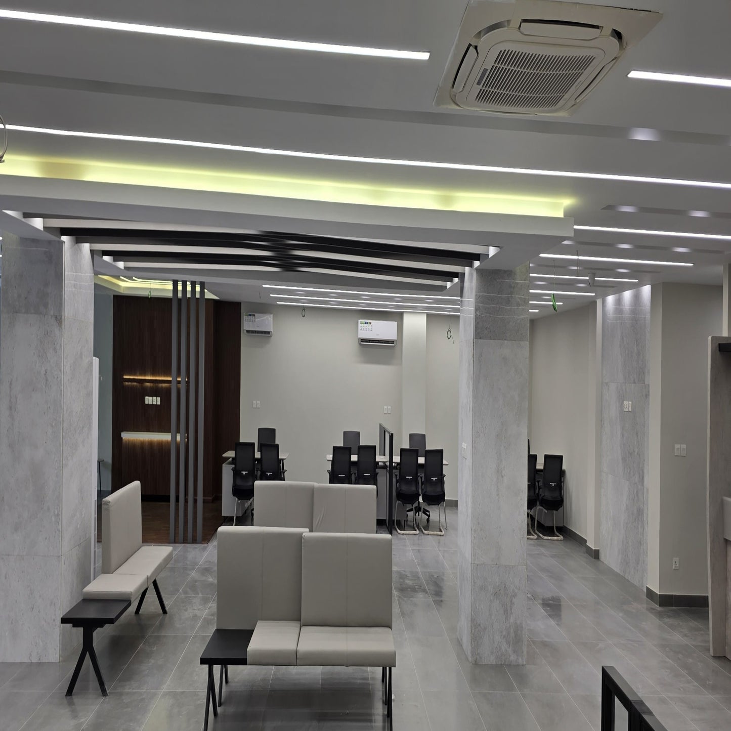 Modern office space with marble walls and floor, beige sofas, and office chairs.