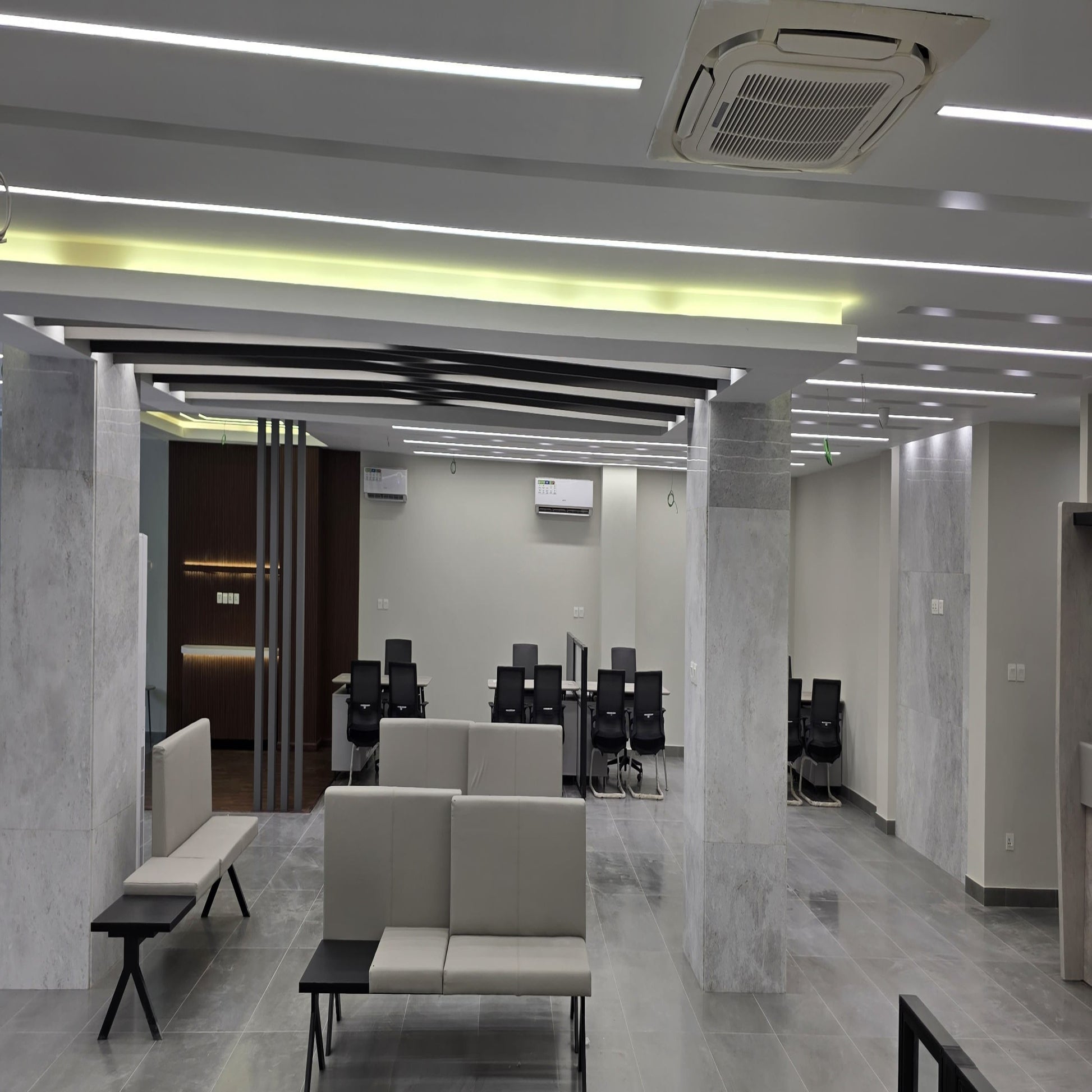 Modern office space with marble walls and floor, beige sofas, and office chairs.